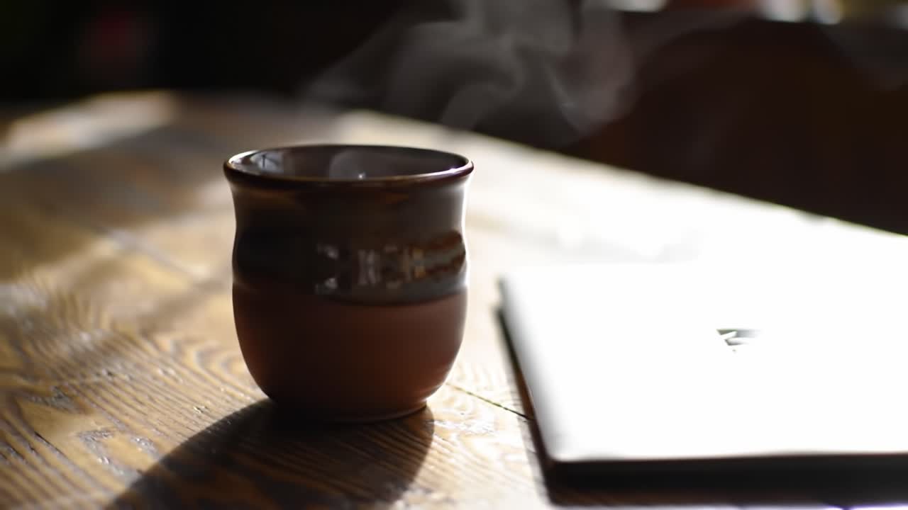 A Serene Moment of Relaxation: A Close-Up of a Warm Mug with Steam Rising on a Calm, Sunlit Table Next to a Laptop, Capturing Cozy Vibes and Morning Comfort