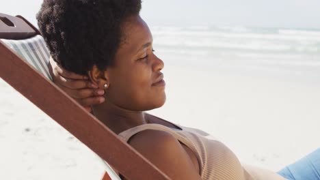 Porträt-Einer-Afroamerikanischen-Frau,-Die-Lächelt-Und-Auf-Einer-Sonnenliege-Am-Sonnigen-Strand-Liegt