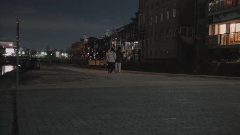 couple strolling along kamo river footpath in kyoto on cold winter night during covid