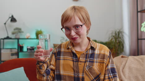 mujer joven sedienta en casa sosteniendo un vaso de agua natural hacer sorbos bebiendo agua tranquila