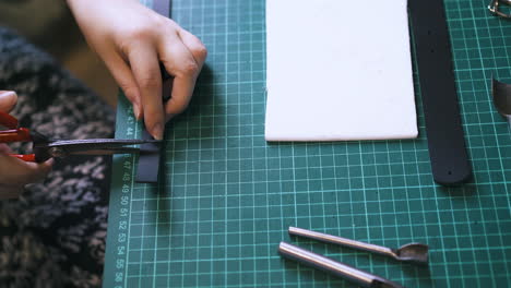 experienced person cuts black leather strip to make garters