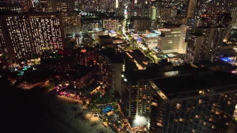 Panorámica-De-30-Fps-De-La-Franja-De-Waikiki-Y-El-Horizonte-Por-La-Noche-Con-Tráfico-De-Palmeras-En-Honolulu-Oahu-Hawaii-En-La-Playa