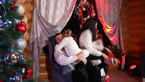 lovely family at home at christmas. pretty little girls embracing their parents. cheerful parents and cute children at the x-mas tree in the living room.