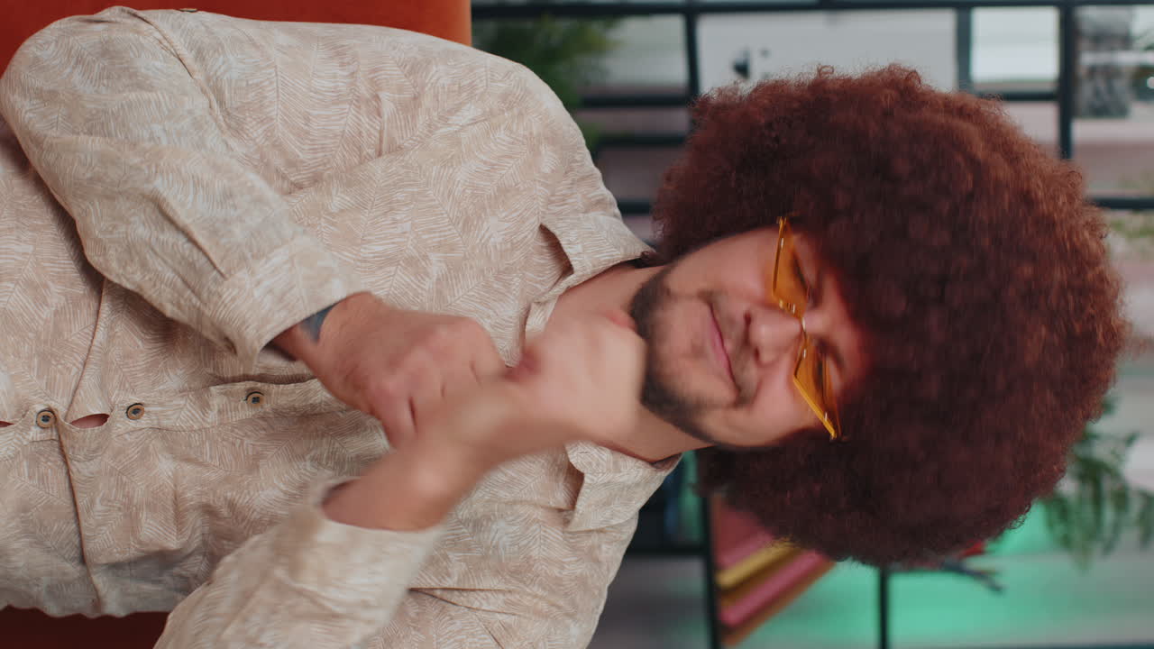 un tipo feliz y relajado con gafas de sol bailando escuchando su música rock n roll favorita en el sofá de casa