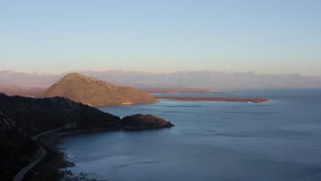 AERIAL---Lake-Skadar-at-sunrise,-blue-sky,-surrounding-mountains,-Montenegro