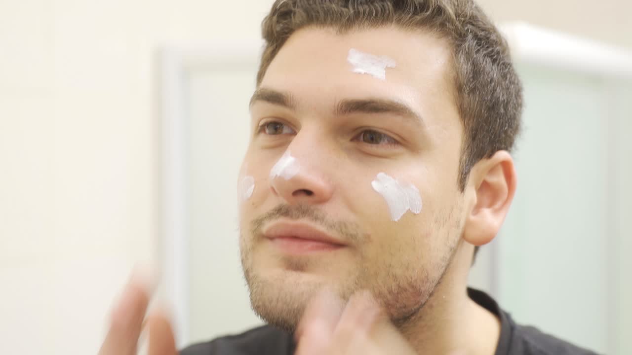 피부 관리: 남자는 화장실에서 얼굴에 크림을 적용하고 있습니다.