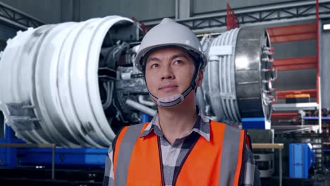 close up of asian male engineer with safety helmet looking around while standing with airplane engine maintenance conducted, analytics checking the turbine