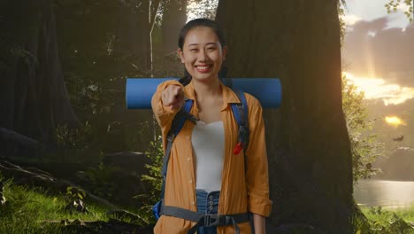 asian female hiker with mountaineering backpack smiling, touching her chest, and pointing to camera while exploring forest nature