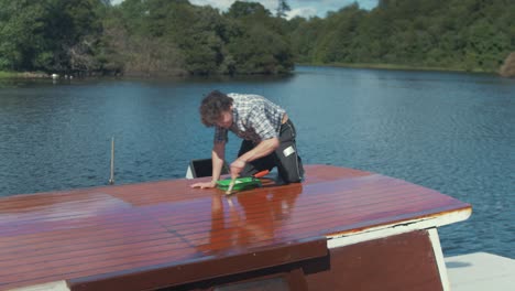 young carpenter rolling on varnish and brushing cabin roof of wood boat