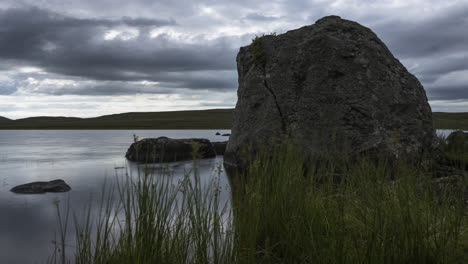 Lapso-De-Tiempo-Del-Lago-Con-Hierba-Y-Grandes-Rocas-En-Primer-Plano-En-Un-Oscuro-Día-De-Verano-Nublado-En-El-Paisaje-Rural-De-Irlanda