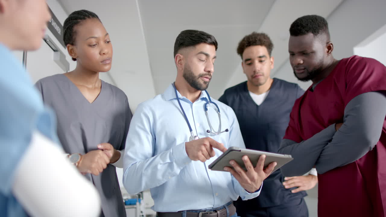 Diverse male and female doctors discussing work using tablet in hospital corridor, slow motion