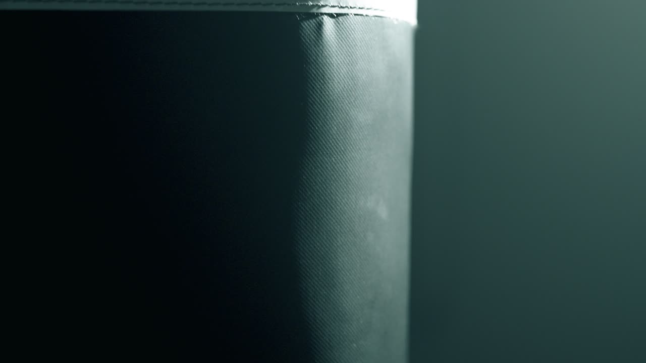 Close-up of black boxing gloves striking a swaying heavy bag. The rhythmic motion and impact create dramatic energy. Moody cinematic lighting emphasizes texture and power in a smoky gym scene