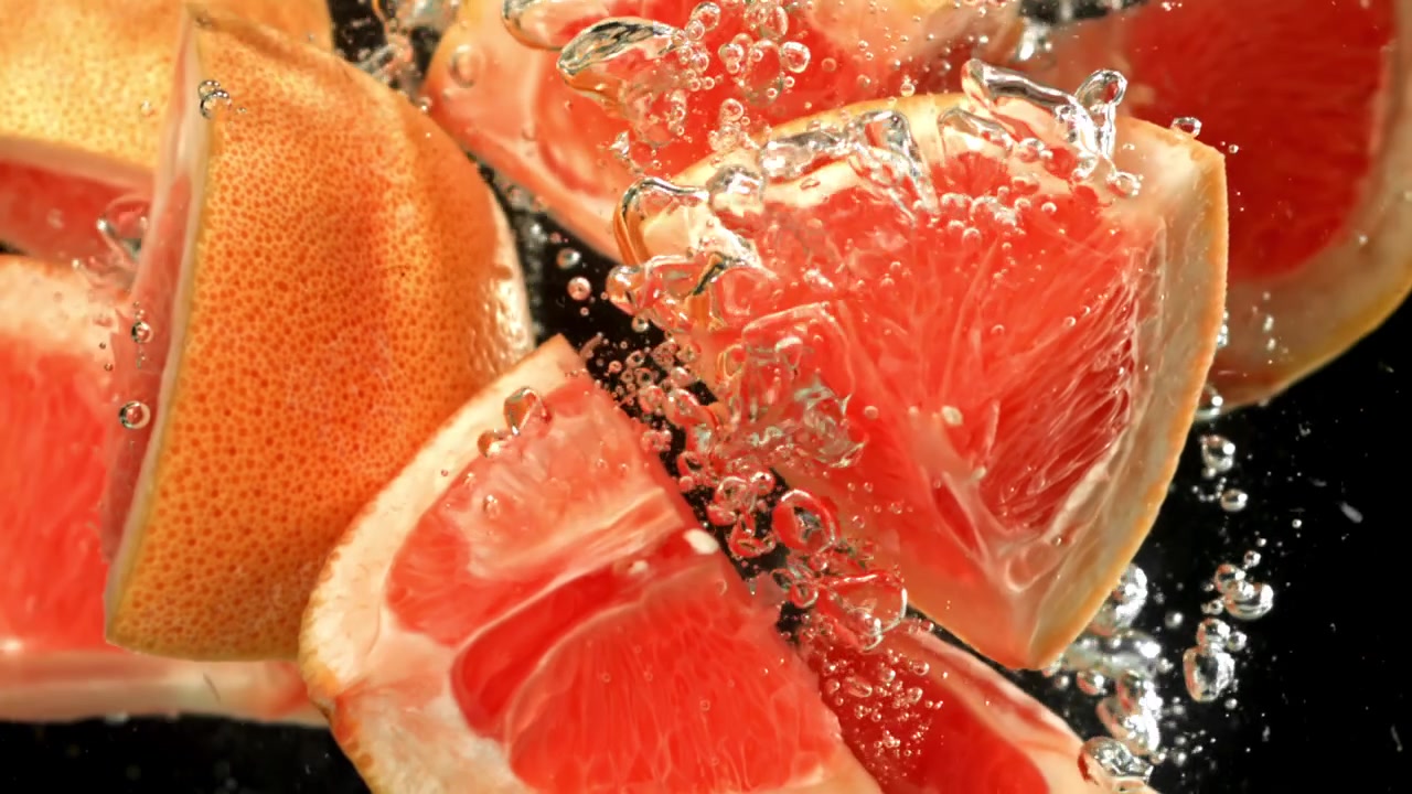 Fette di pompelmo fresco che cadono nell'acqua con bolle su sfondo nero