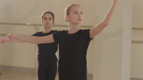 a group of young ballet students in black dancewear practicing positions in a spacious ballet studio with wooden flooring and wall-mounted barres. focused expressions and synchronized movements.