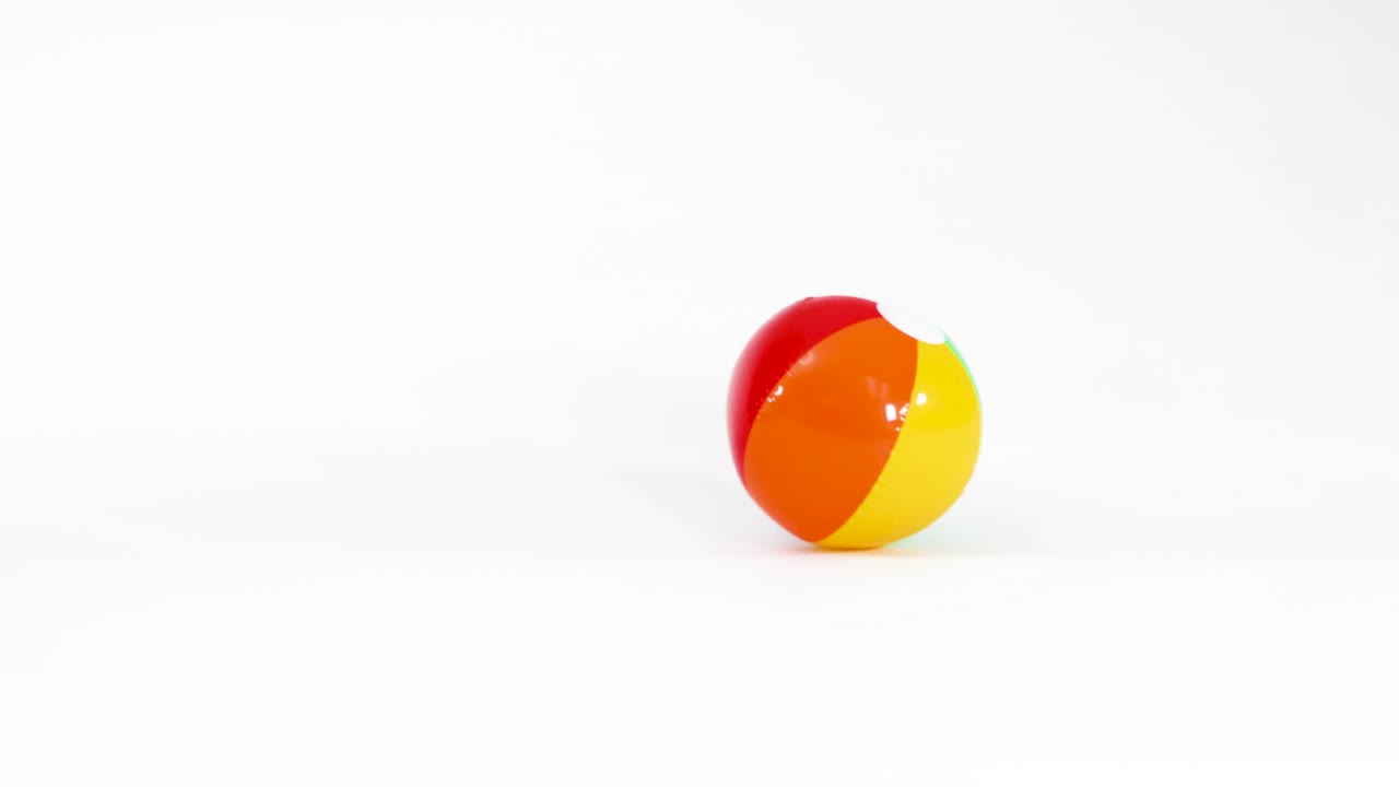 A multi-colored inflatable beach ball bounces and rolls across a clean white studio background