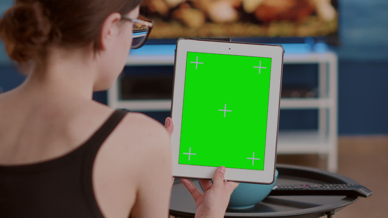 Closeup of young woman holding vertical digital tablet with green screen in online conference or group video call