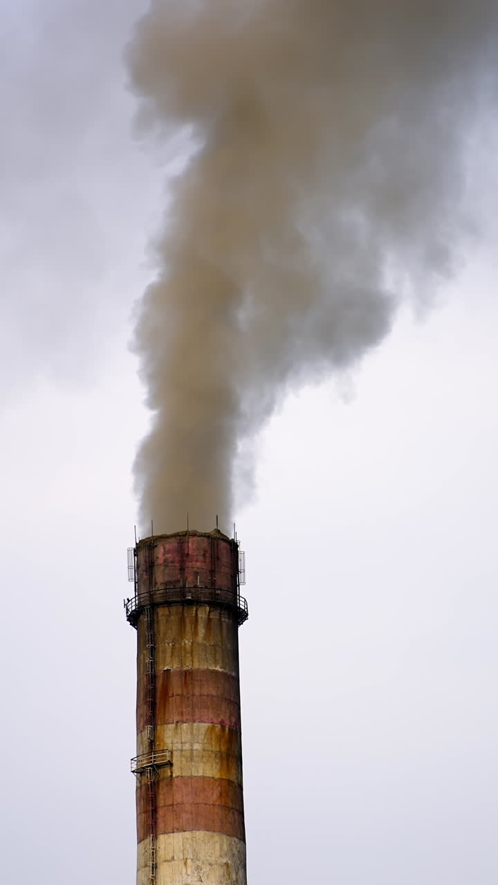 Smokestack exhausting combustion gases into the air. Dense smoke from pipes pollute the atmosphere. Dangerous emissions in the sky. Climate change. Vertical video