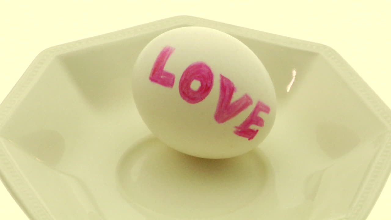 la mano de una mujer levanta y aplasta un huevo en un bol con la palabra amor escrita en él