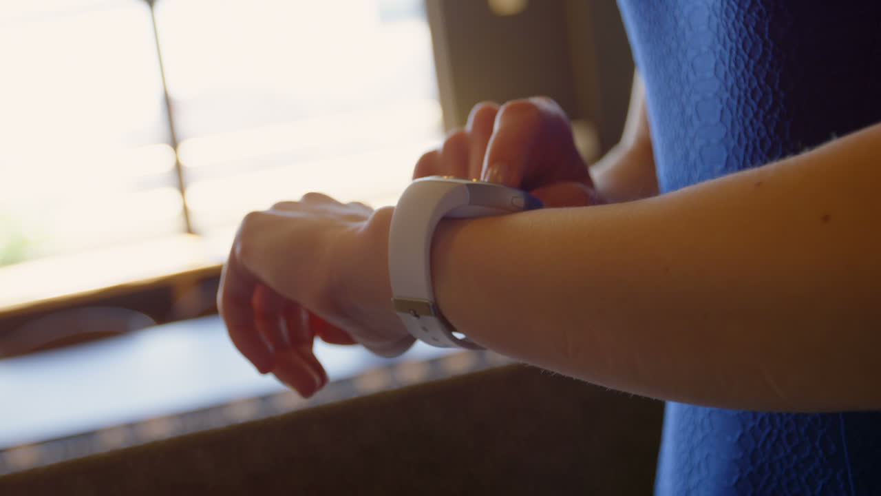 Primo piano di una giovane donna d'affari che controlla il suo smartwatch e usa il telefono cellulare in un moderno ufficio 4k