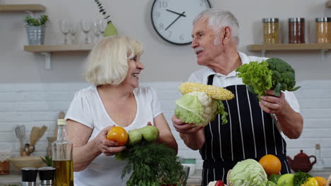 senior grandparents couple in kitchen. mature man and woman recommending eating raw vegetable food