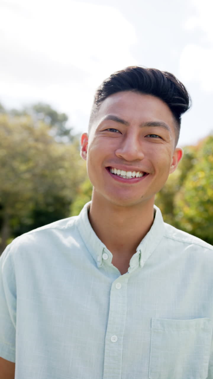 Vertical video of, portrait of happy asian man smiling in garden, slow motion