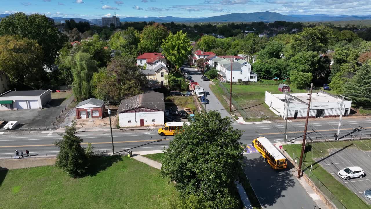Aerial tracking shot of several yellow school buses on junction of american neighborhood at sunny day. Colored trees in autumn season