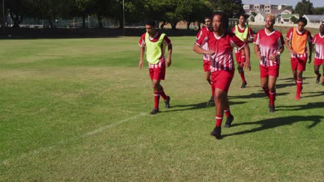 video of diverse group of male football players warming up on field, running