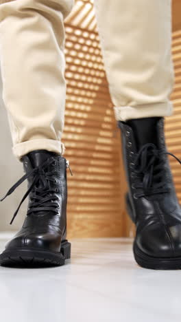 woman in light jeans presents the black footwear with laces. modern boots on a plain sole and rounded nosepieces close up. studio backdrop.