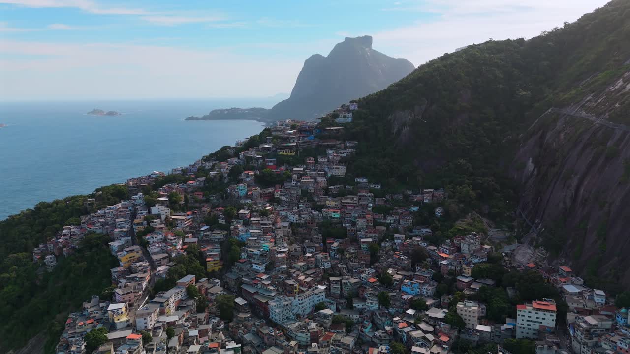 Aerial ascend reveals Favela Vidigal's stacked hillside homes above coastal Rio de Janeiro
