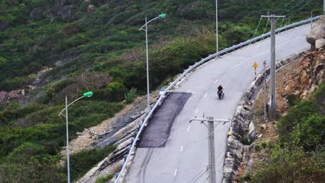 Tracking-shot-driving-up-a-curvy-road-on-motorbike-carrying-kite-surfing-board,-watersports-session-trip