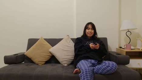 Portrait-of-a-cute,-Filipino-girl-smiling-and-laughing-on-the-couch-while-watching-television