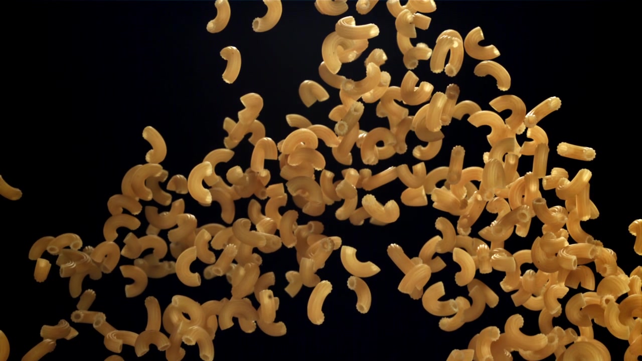 Rallentatore di pasta maccheroni cruda che cade su sfondo nero.