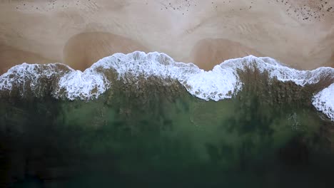 bird's eye view of waves crashing on the coastline of an empty beach, aerial