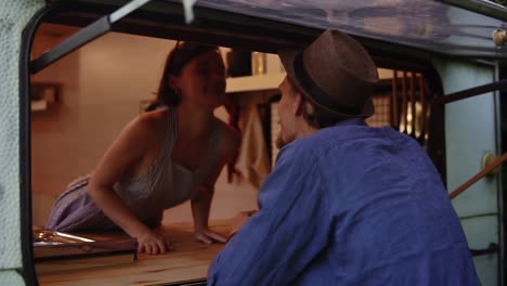 man in a hat and blue shirt came to the window in trailer truck, house on wheels and sensually kiss his wife through it. concept of vacation or life in a van