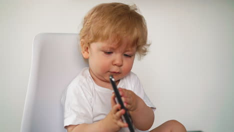 little-boy-plays-with-black-mobile-phone-sitting-on-chair