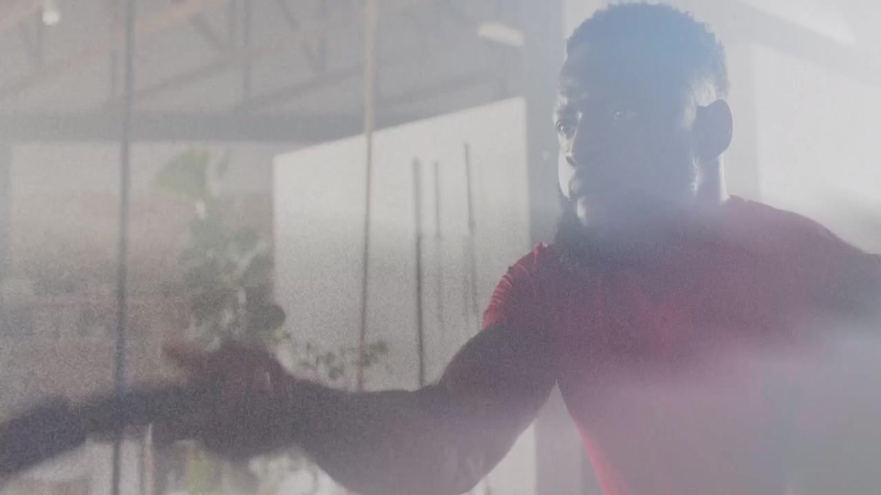 Man in red shirt gripping battle rope, creating alternating waves in loft gym, training for fitness