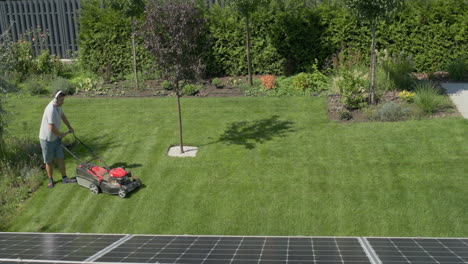 a middle-aged man mows the lawn in the backyard of his house. listening to music with headphones