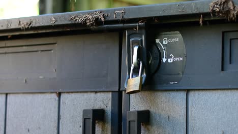 beautifully shot alternate angle close up of a padlock and latch on a shed with hands reaching in to wrench and pull at the lock in an attemp to break in, with stylish bokeh