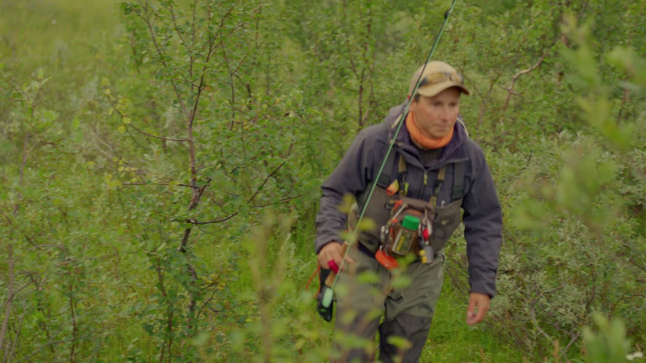 Close view of man with fishing gear walking in green bushy landscape