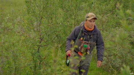 close view of man with fishing gear walking in green bushy landscape