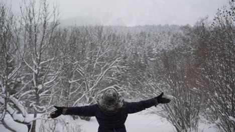 anonymous woman in outerwear outstretching arms in winter forest