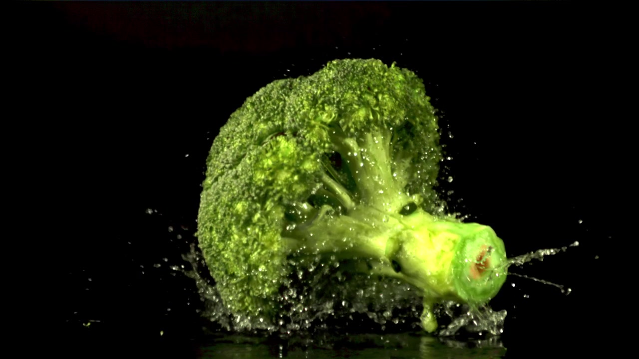 Broccoli freschi che cadono e schizzano acqua su sfondo nero