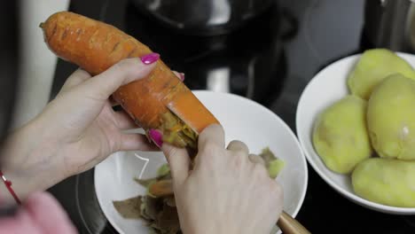 las manos de la ama de casa pelando zanahorias en la cocina.