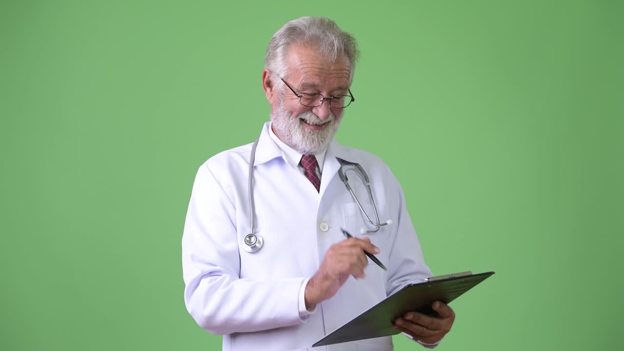 Handsome senior bearded man doctor against green background