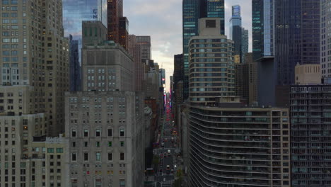 Forwards-fly-above-wide-street-between-downtown-skyscrapers.-Red-brake-lights-of-cars-in-distance.-Manhattan,-New-York-City,-USA