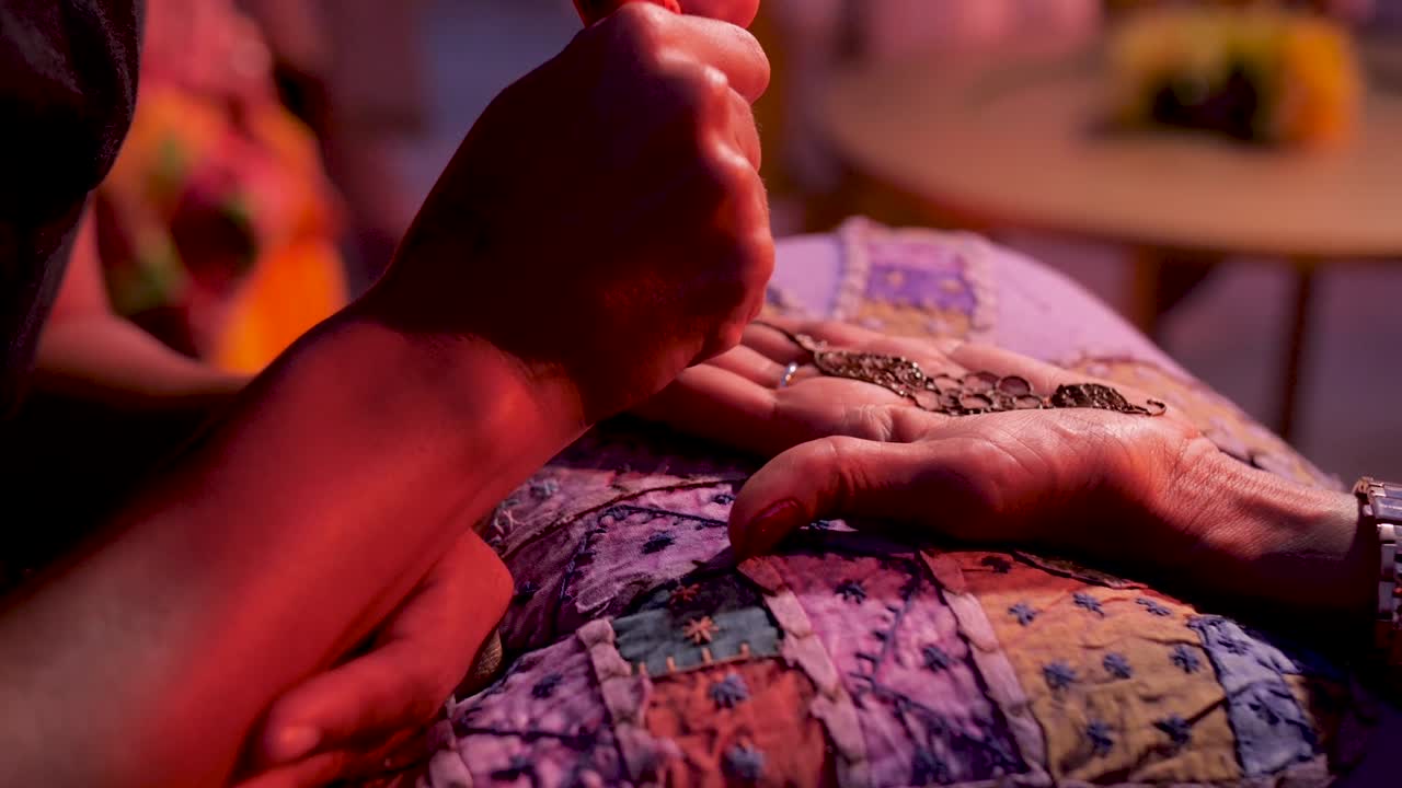 manos sobre una almohada bordada mientras un artista pinta intrincados símbolos con henna