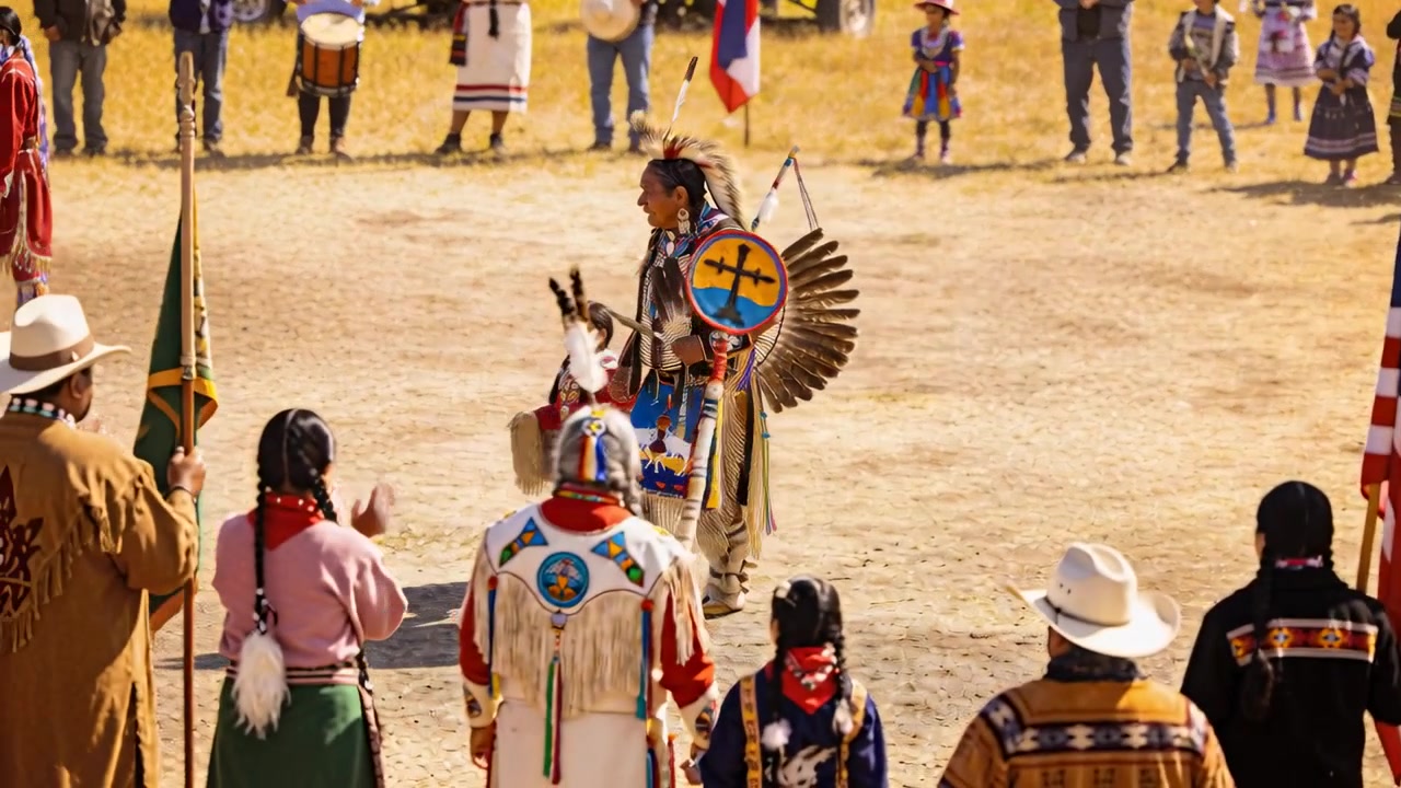 Trommeln beginnt, Tänzer in traditioneller Kleidung und Kind überqueren ein zeremonielles Feld, halten einen Bustle für ein Ritual.