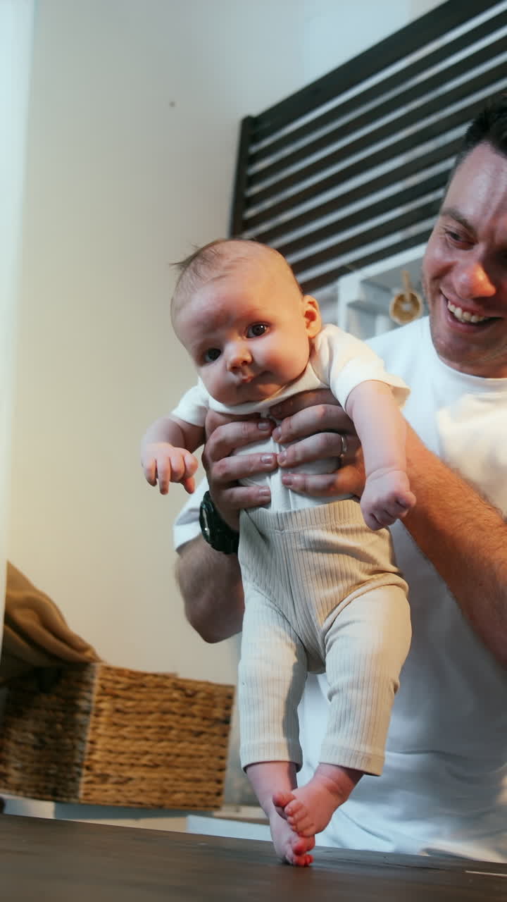 Muscular Caucasian man holds in a hands his tiny son. Daddy puts an infant on the wooden table so the kid's feet touch the surface. Vertical video