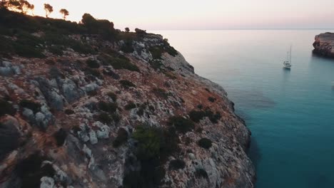 Imágenes-Aéreas-De-Un-Amanecer-En-Una-Bahía-Vacía-Con-Veleros-En-El-Tranquilo-Mar-Mediterráneo-En-Mallorca,-España