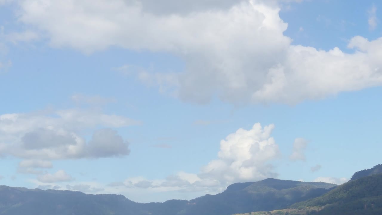 A serene view of rolling hills beneath a sky dotted with fluffy clouds.